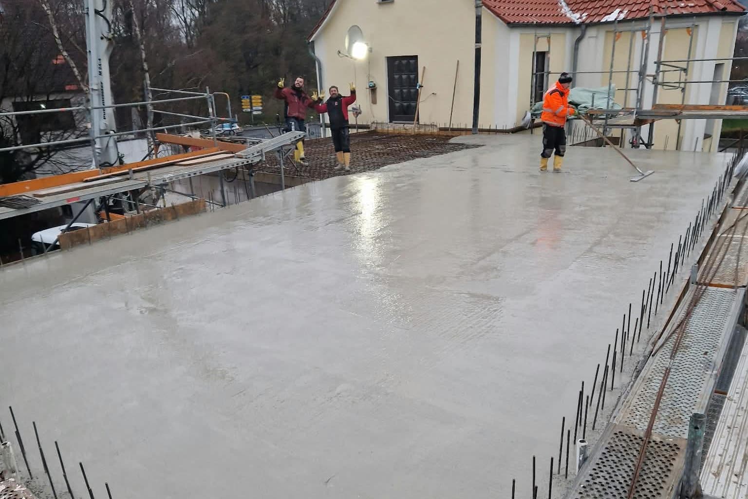 Frisch betonierte Geschossdecke, Mitarbeiter ziehen den Beton ab, am Rand die Anschlussbewehrung